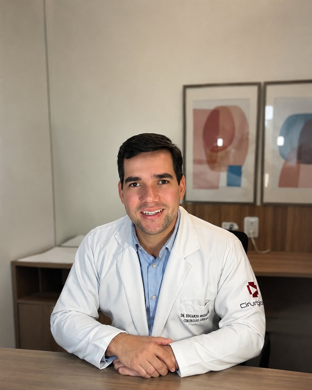 Dr. Eduardo Medeiros de jaleco da Cirurgia Já, sentado à mesa do consultório